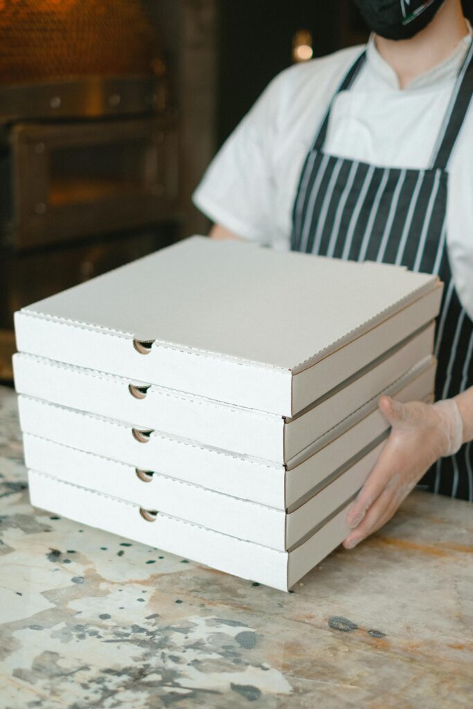 pexels-photo-5953555-5953555 A pizza delivery worker holds stacked boxes in a restaurant kitchen, ready for delivery.